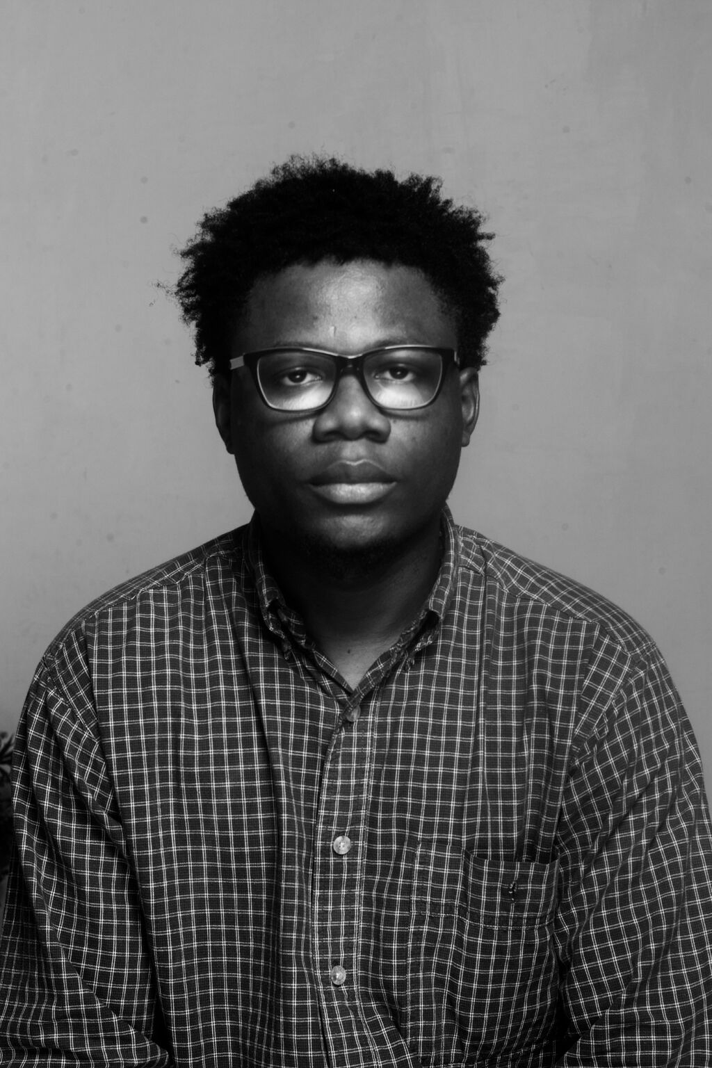 Black-and-white portrait of Amedu Isaiah, editor and founder of CutReel Pro, wearing glasses and a checked shirt